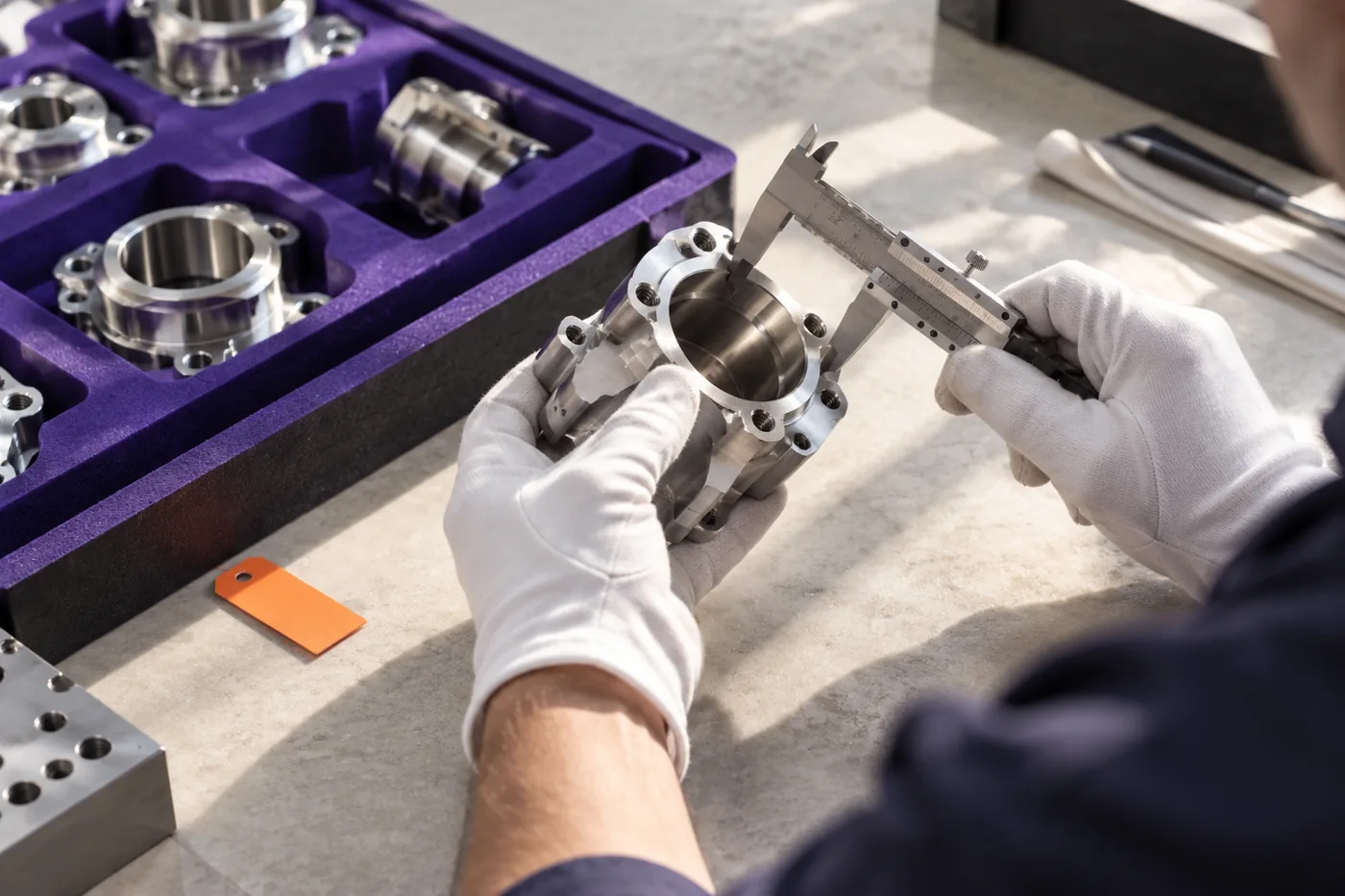 Gloved hands measure a machined part during an inspection.